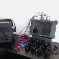 Portable electrical tester with multicolored cables, alligator clips, and carrying case on table.