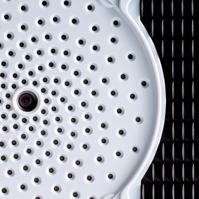 Close-up of a white circular object with holes next to a black grid surface.