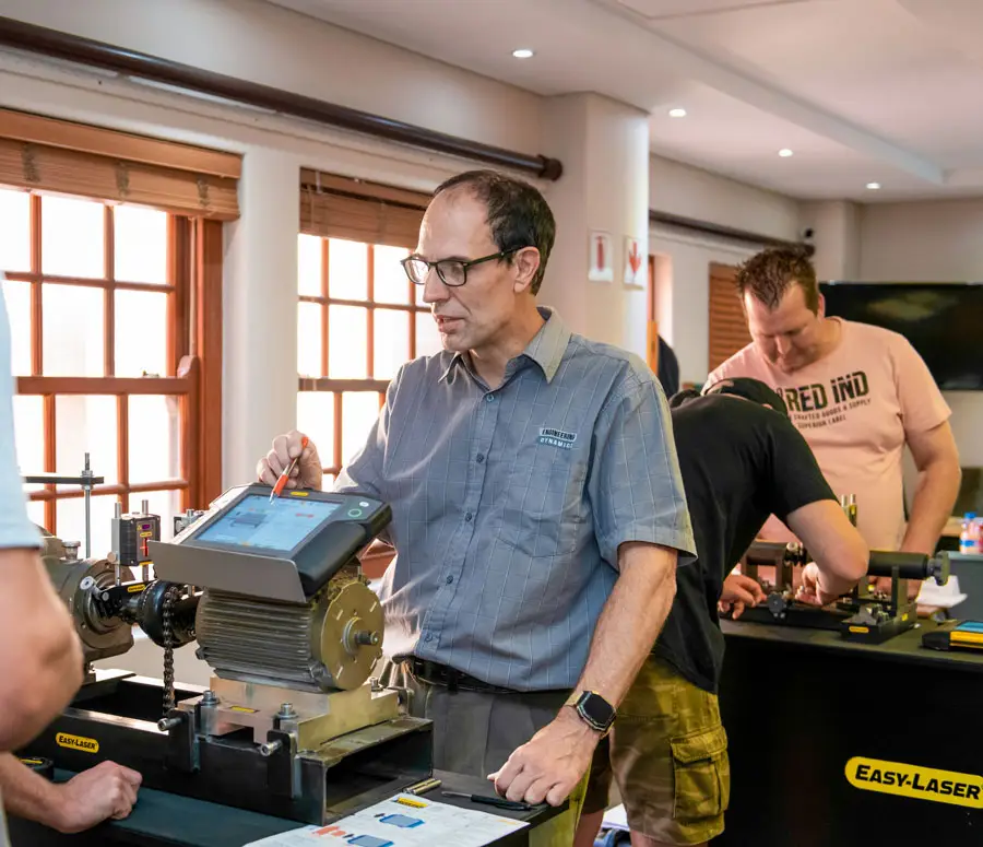 Man using machine alignment tool on motor in bright training room.