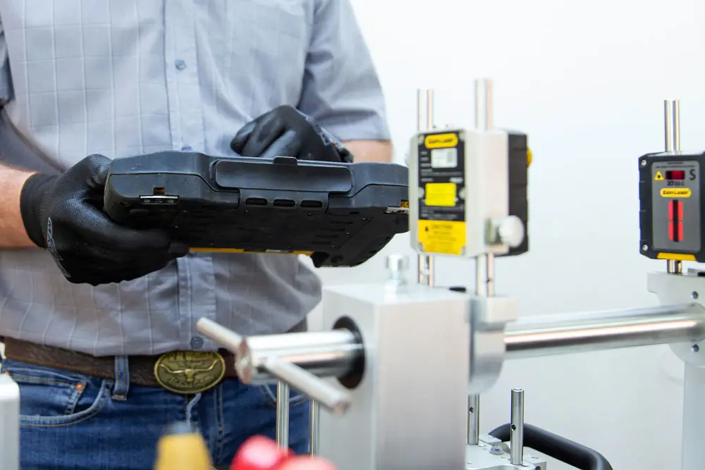 "Technician in gray shirt and gloves holding device near measurement instruments on industrial workbench"