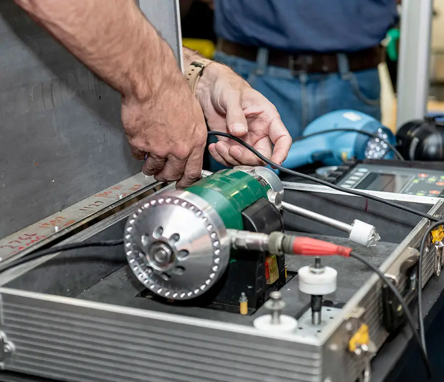 Hands connecting wires to a green electric motor inside an open metal case.