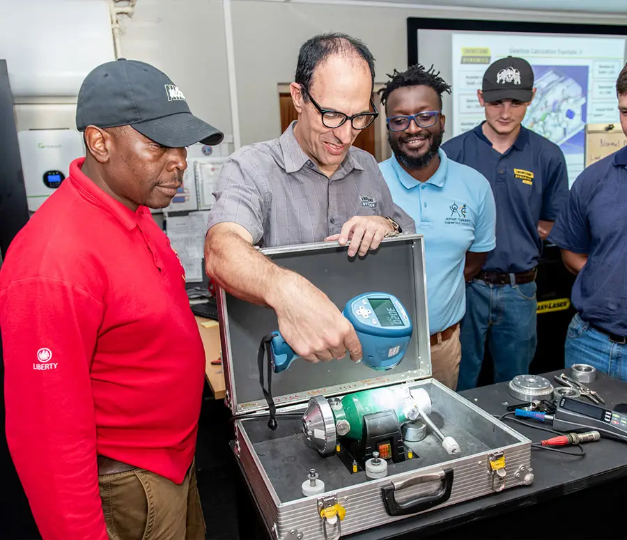 "Group of five individuals observing technical equipment demonstration with digital display in lab setting"