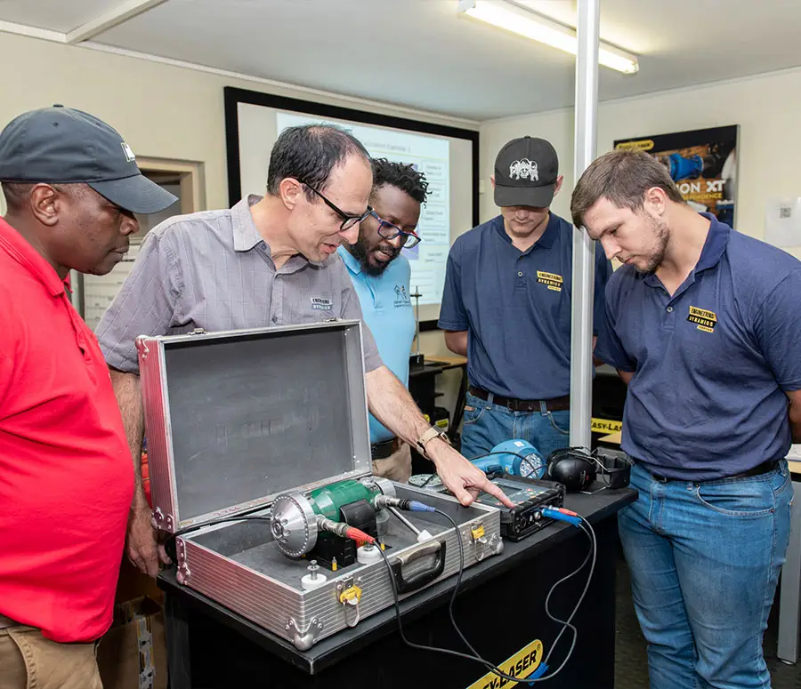 "Group of trainees observing technical workstation with instructor demonstrating electrical and mechanical components"