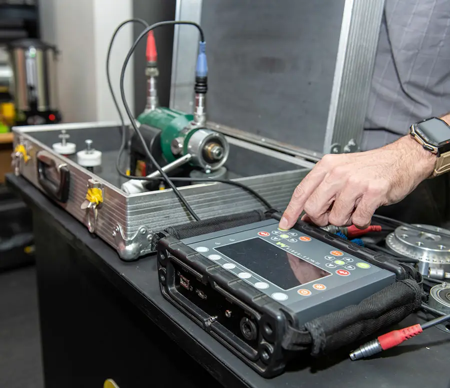 "Technician operating portable ultrasonic testing device with probe on metallic component in carrying case"