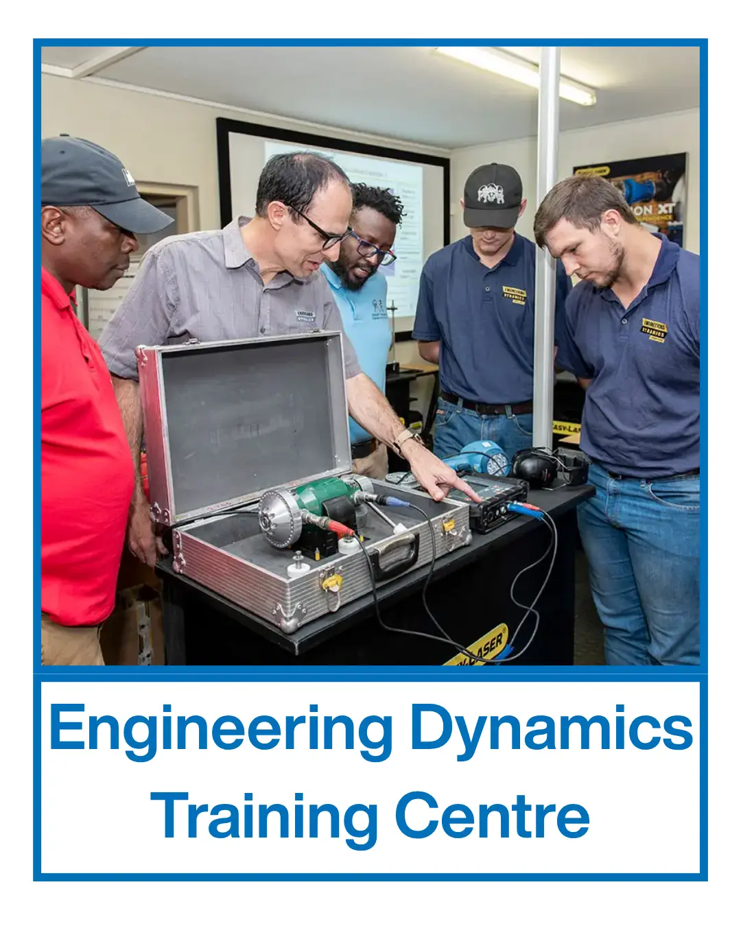 Five men stand around an open equipment case with machinery, engaging in an Elementor demonstration at the Engineering Dynamics Training Centre.